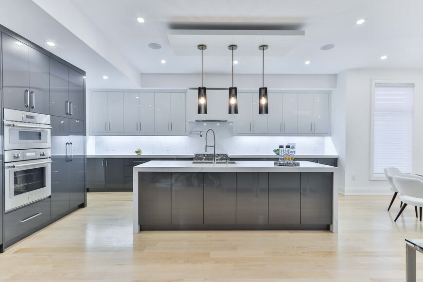 Alea modular kitchen – modern modular kitchen with a grey and white high-gloss finish, spacious island, built-in appliances, and stylish pendant lights, blending aesthetics with functionality.