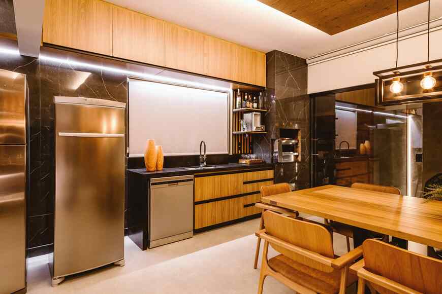 Modern kitchen featuring sleek cabinets, stainless steel appliances, a wooden dining table, and stylish pendant lighting.