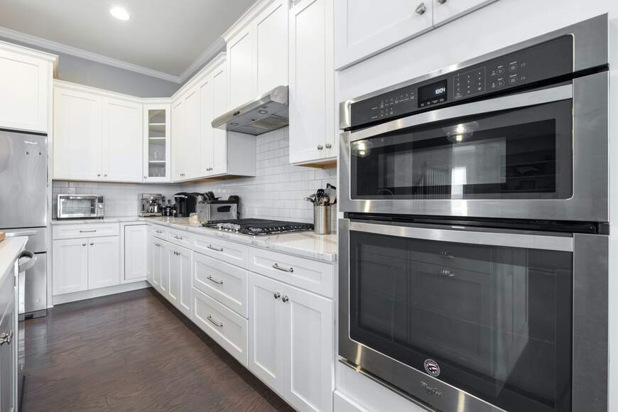 Modern white modular kitchen by alea modular kitchen, featuring shaker-style cabinets, built-in stainless steel double ovens, and a sleek gas cooktop. The design includes a subway tile backsplash, quartz countertops, and smart storage solutions, offering a perfect blend of style and functionality.