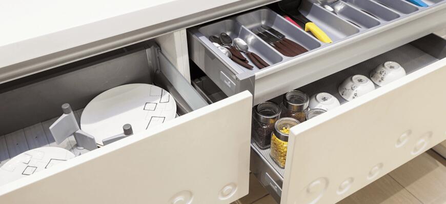 Modular kitchen accessories that you must have 1 Modern kitchen drawers opened, revealing organized cutlery, cooking utensils, and jars of food alongside round plates.