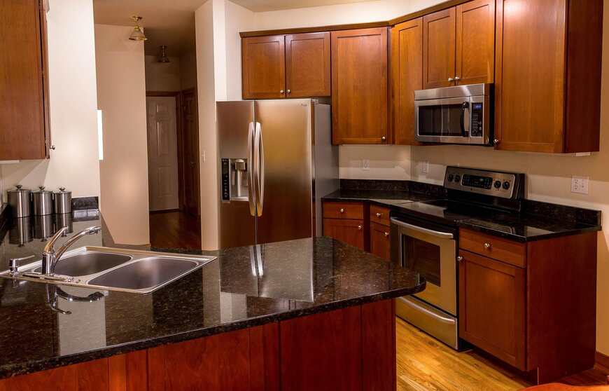 Modular kitchen cabinets: the ultimate guide 2 Elegant modular kitchen by alea modular featuring rich wooden cabinetry, polished black granite countertops, and built-in stainless steel appliances. A timeless kitchen design with ample storage and a functional island sink for modern homes.